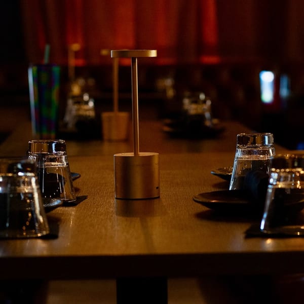 A dimly lit table at The Sea restaurant, set with glasses, plates, and a modern gold lamp.