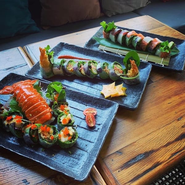 Three plates of colorful sushi rolls, including lobster and shrimp, on a rustic wooden table.