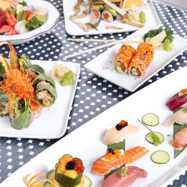 An overhead view of various sushi and sashimi dishes on white plates, including rolls, nigiri, and spring rolls.