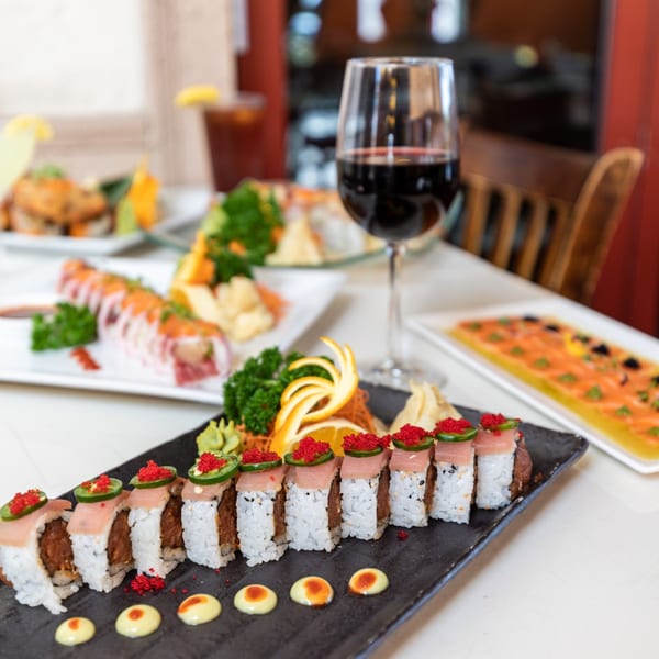 Sushi rolls with tuna, jalapeño, and red tobiko, alongside other Asian dishes and wine.