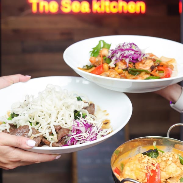 Hands holding two bowls of Asian cuisine, with a third dish in the foreground.