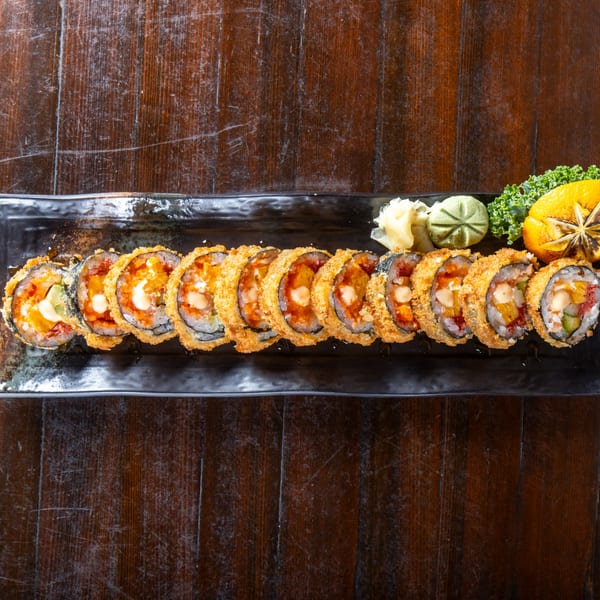 A long black plate of crispy fried sushi rolls with garnishes on a dark wooden table.