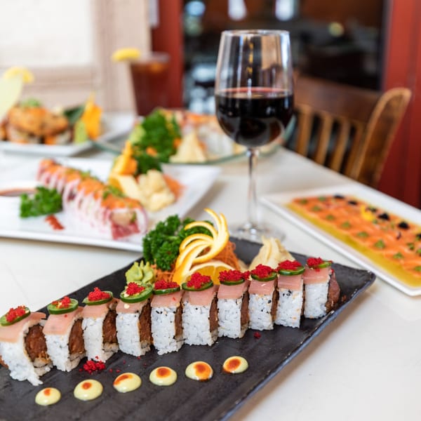 A black platter of tuna sushi rolls with red roe and jalapeño, alongside other Asian dishes and wine.