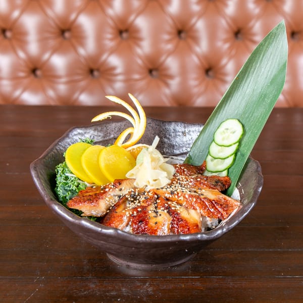 Unagi donburi with grilled eel, pickled radish, ginger, and cucumber, on a wooden table.