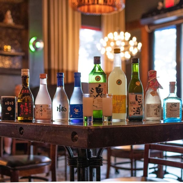 A variety of sake bottles and two shot glasses filled with sake on a dark wooden table.