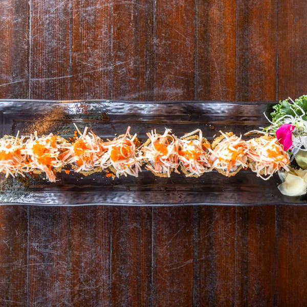 Fried sushi rolls topped with crab, mayonnaise, and orange tobiko, served on a black plate.